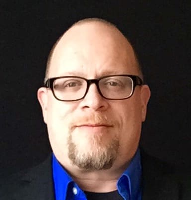 A man with glasses and beard wearing a suit.